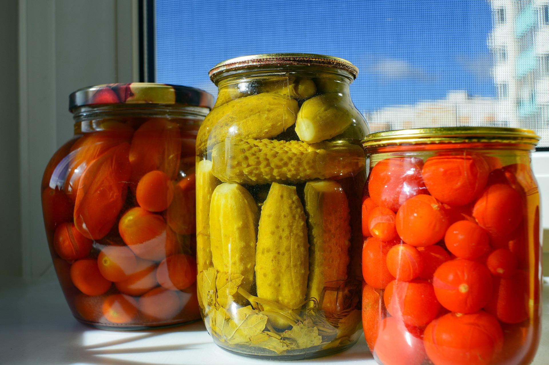 three jars of pickled items on a table. tomatoes, pickles and cherry tomatoes 